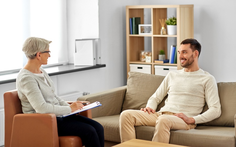 psychology, mental therapy and people concept - smiling senior woman psychologist with clipboard talking to young man patient at psychotherapy session