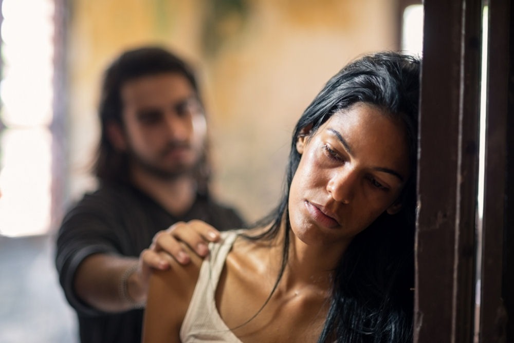 man placing a hand on a woman's shoulder as she leans in the doorway