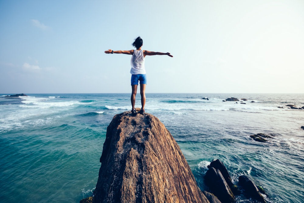 woman standing on a rock in the waves of the ocean