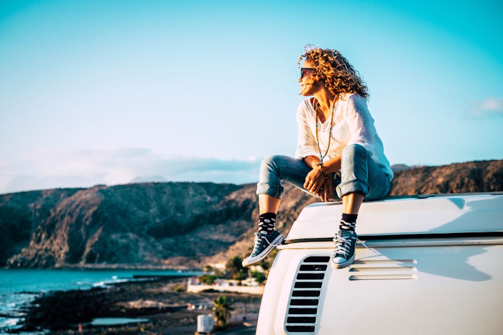 woman sitting on top of a van looking at the coastline