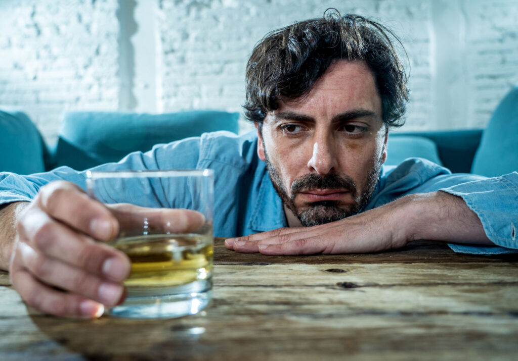 man resting his head on the table and looking at a glass with alcohol