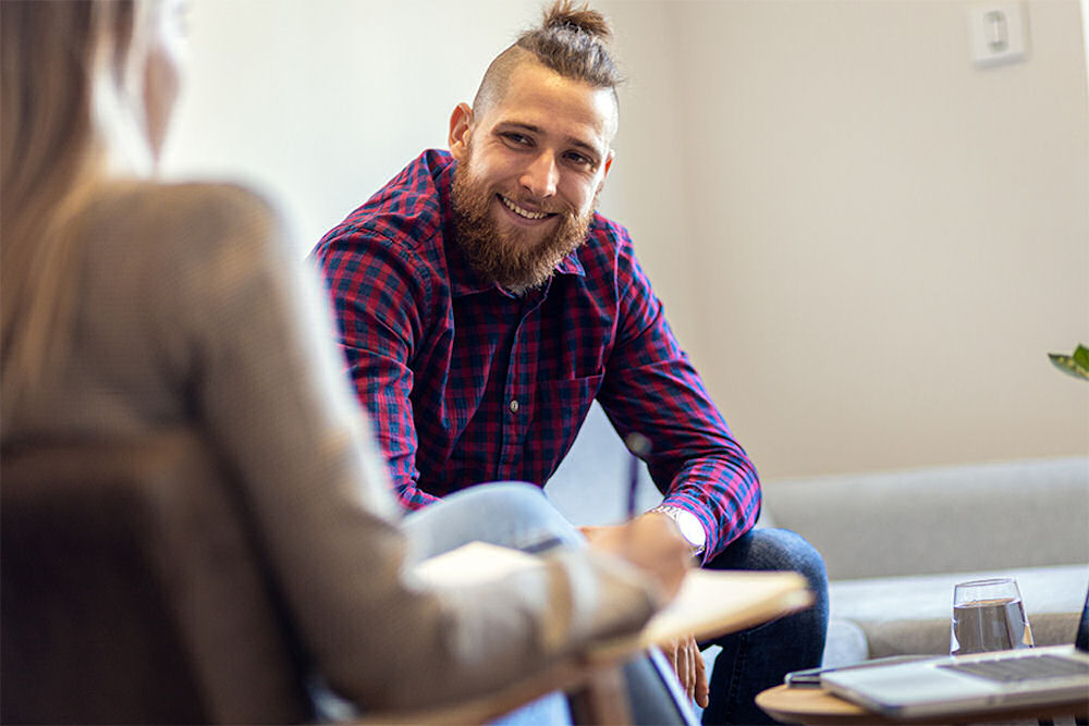 young man sitting on couch near therapist who is taking notes