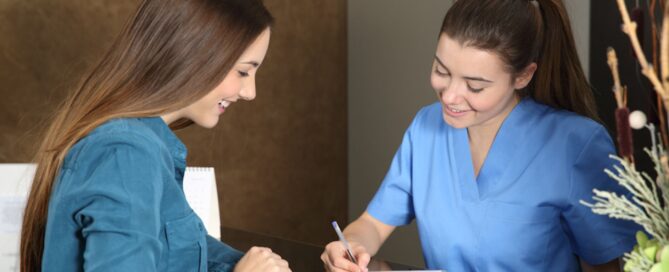 A woman in a blue shirt smiles while speaking with a receptionist in blue scrubs, who is filling out a form at the front desk of a drug rehab facility in Los Angeles. Both appear to be at ease in this welcoming rehab setting.